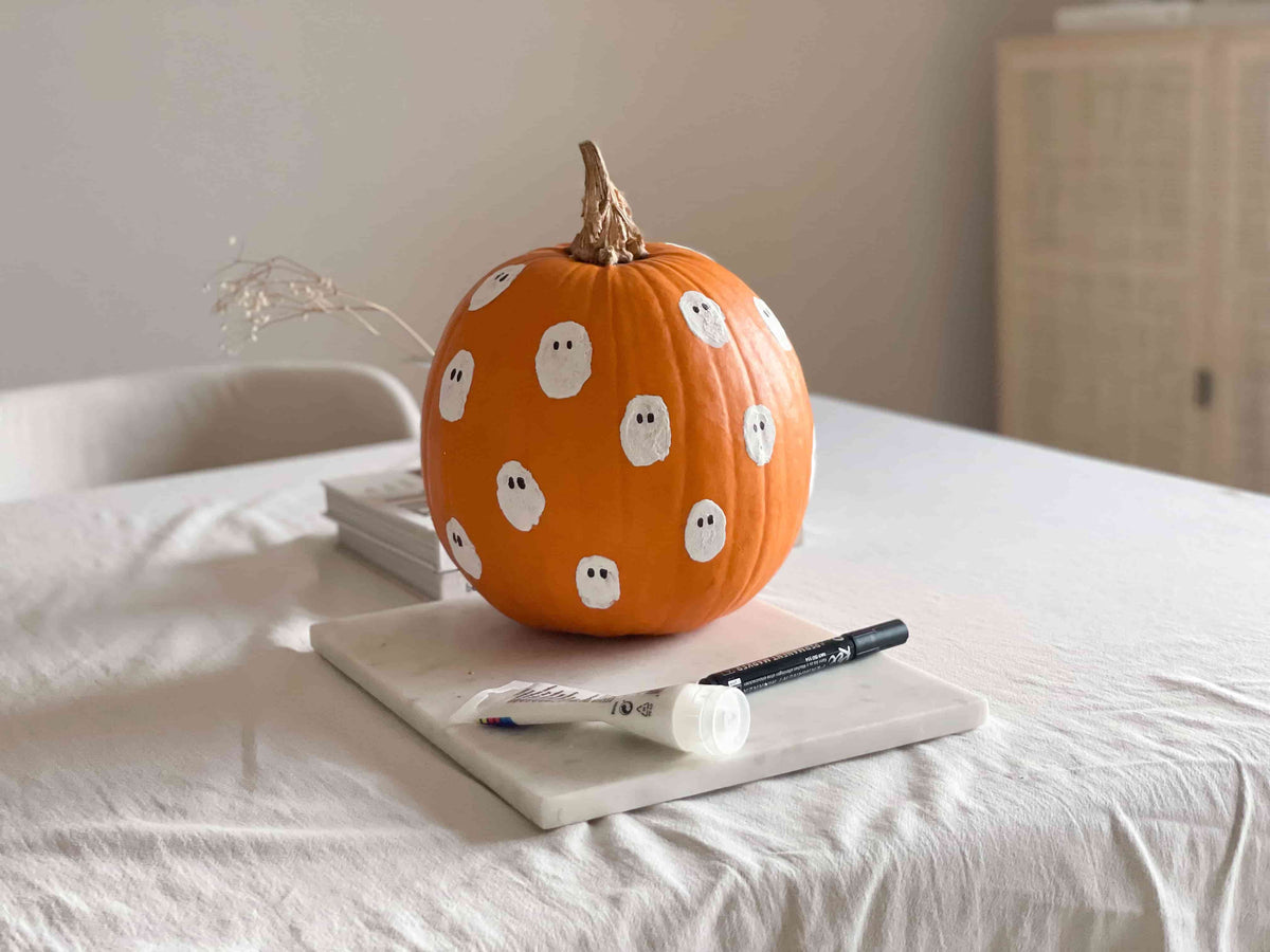 Fertig bemalter Halloween Kürbis mit weißen Geister-Motiven und schwarzen Augen.