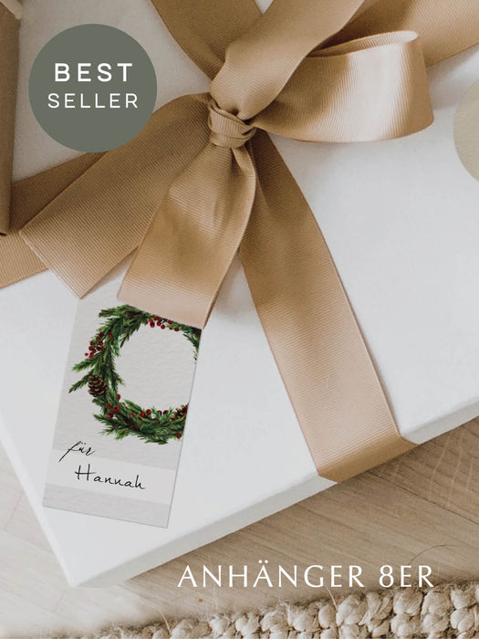 Geschenkanhänger mit grünem Weihnachtskranz und Namenszeile, im skandinavischen Design – angebracht an einem verpackten Geschenk.