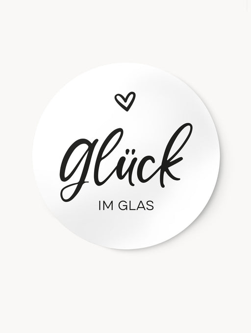 Rundes, selbstklebendes Etikett mit der Aufschrift Glück im Glas und einem Herzmotiv im Schwarz-Weiß Design.