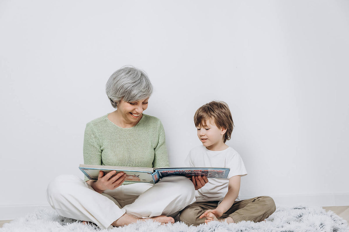 Oma mit ihrem Enkel sitzen nebeneinander und lesen gemeinsam ein Buch