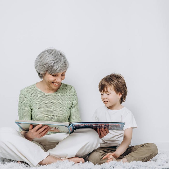 Oma mit ihrem Enkel sitzen nebeneinander und lesen gemeinsam ein Buch