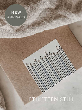 Rechteckiger Aufkleber mit Kerzenmotiv im hellblauen, beigefarbenen Design verschließt eine braune Faltschachtel über die Kante, wodurch ein stilvolles, elegantes Verpackungsdesign entsteht.