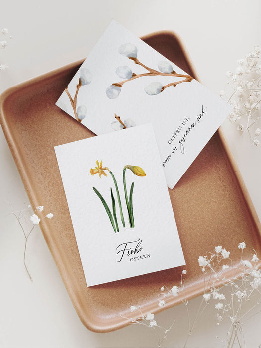 Hochwertige Osterkarten mit der Aufschrift "Frohe Ostern" und "Ostern ist, wenn wir zusammen sind" im nordischen, eleganten Design aus Naturkarton, liegend auf einem braunen Keramik-Tablett.