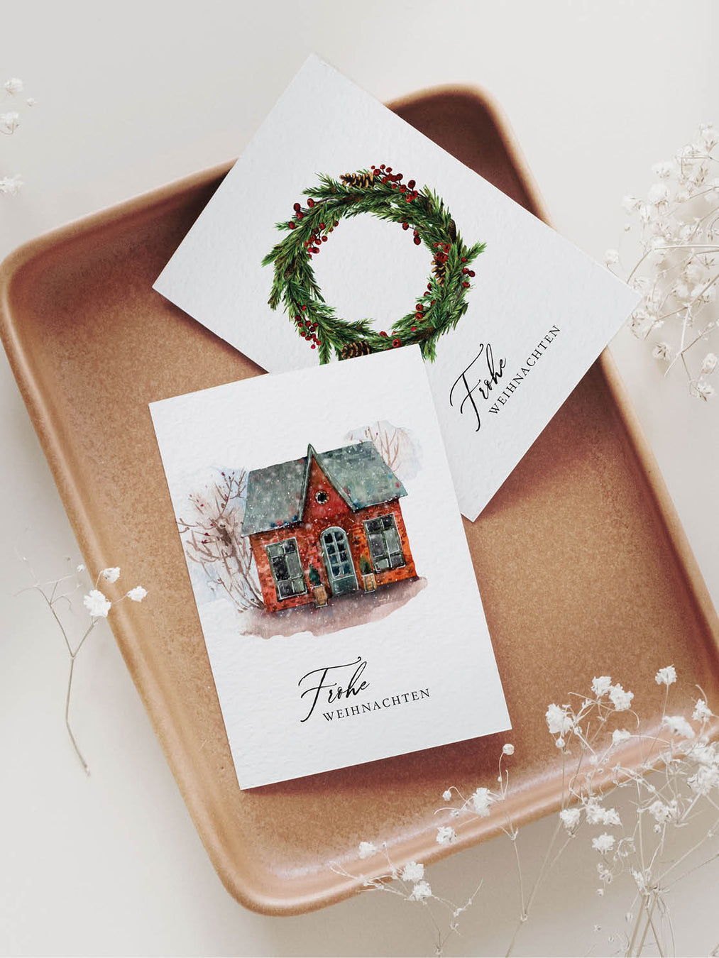 Zwei Weihnachtskarten im nordischen Stil und der Aufschrift "Frohe Weihnachten" aus Naturkarton, liegend auf Keramik-Tablett.